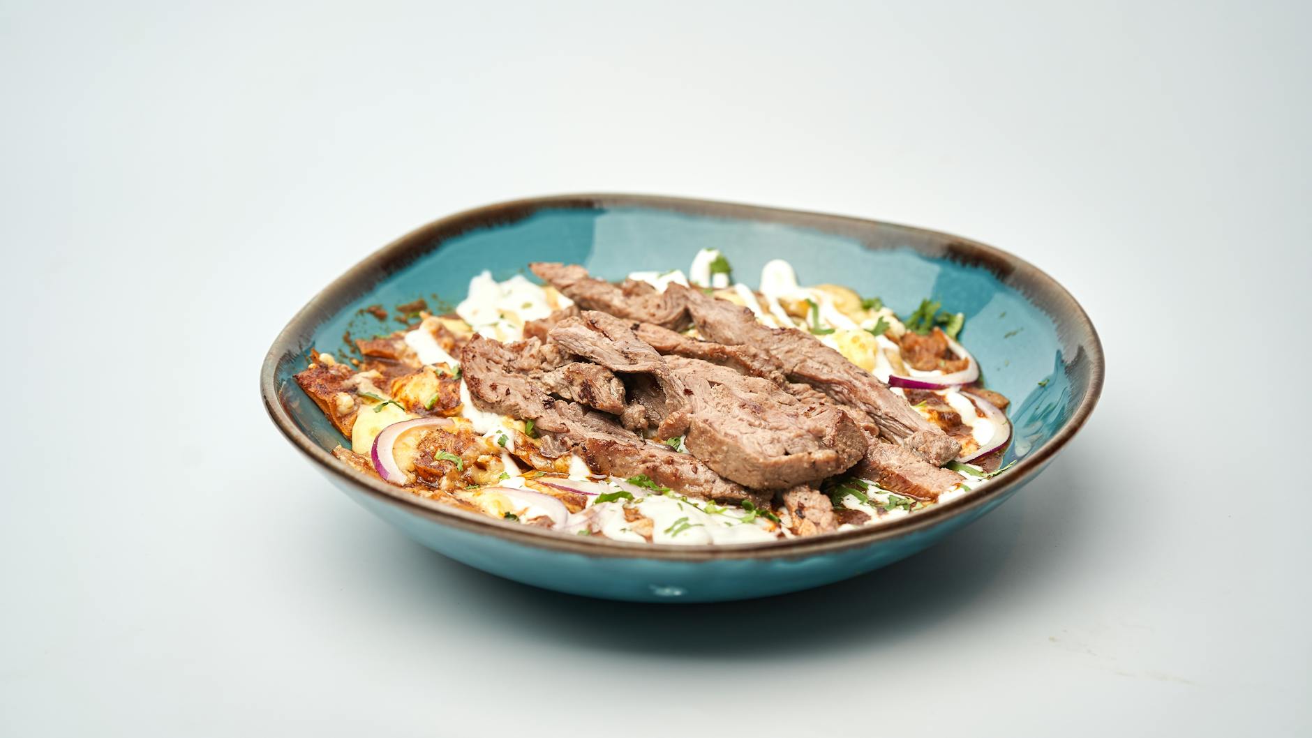 Kawałki baraniego kebaba w niebieskiej misce z cebulą i sosem czosnkowym