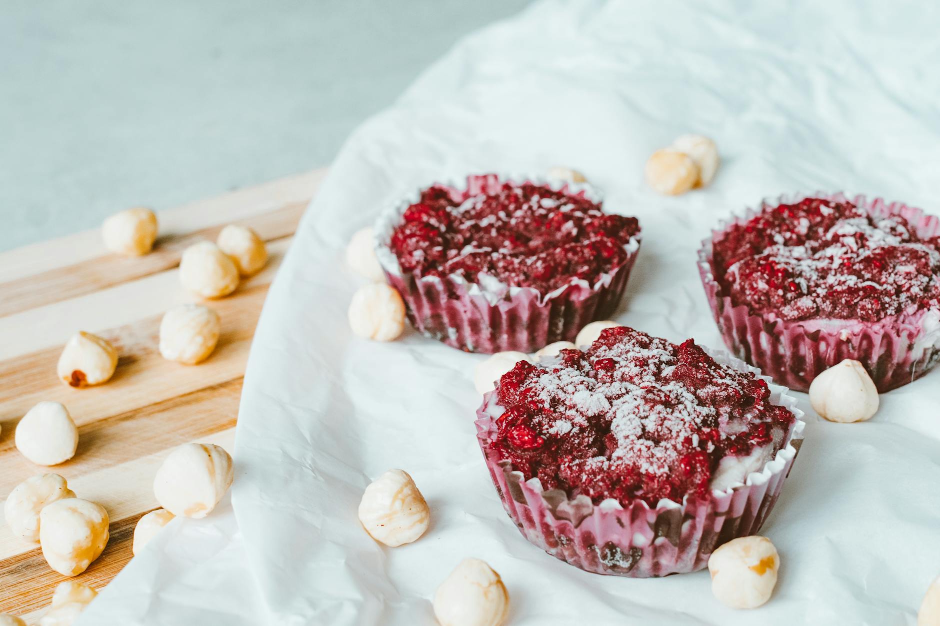 Malinowe muffinki posypane cukrem na pergaminie z orzechami laskowymi