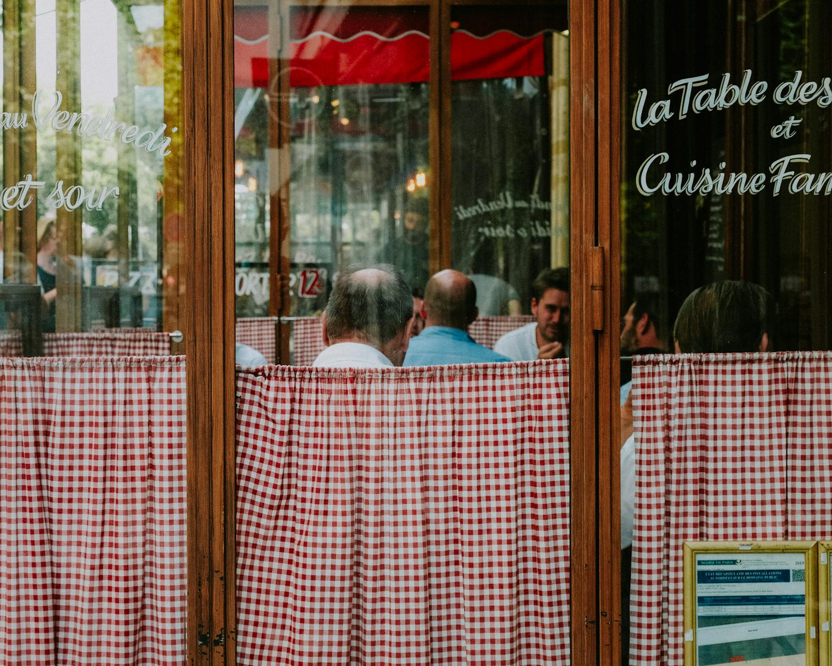 Goście jedzą w francuskiej restauracji za szybą z czerwonymi zasłonami